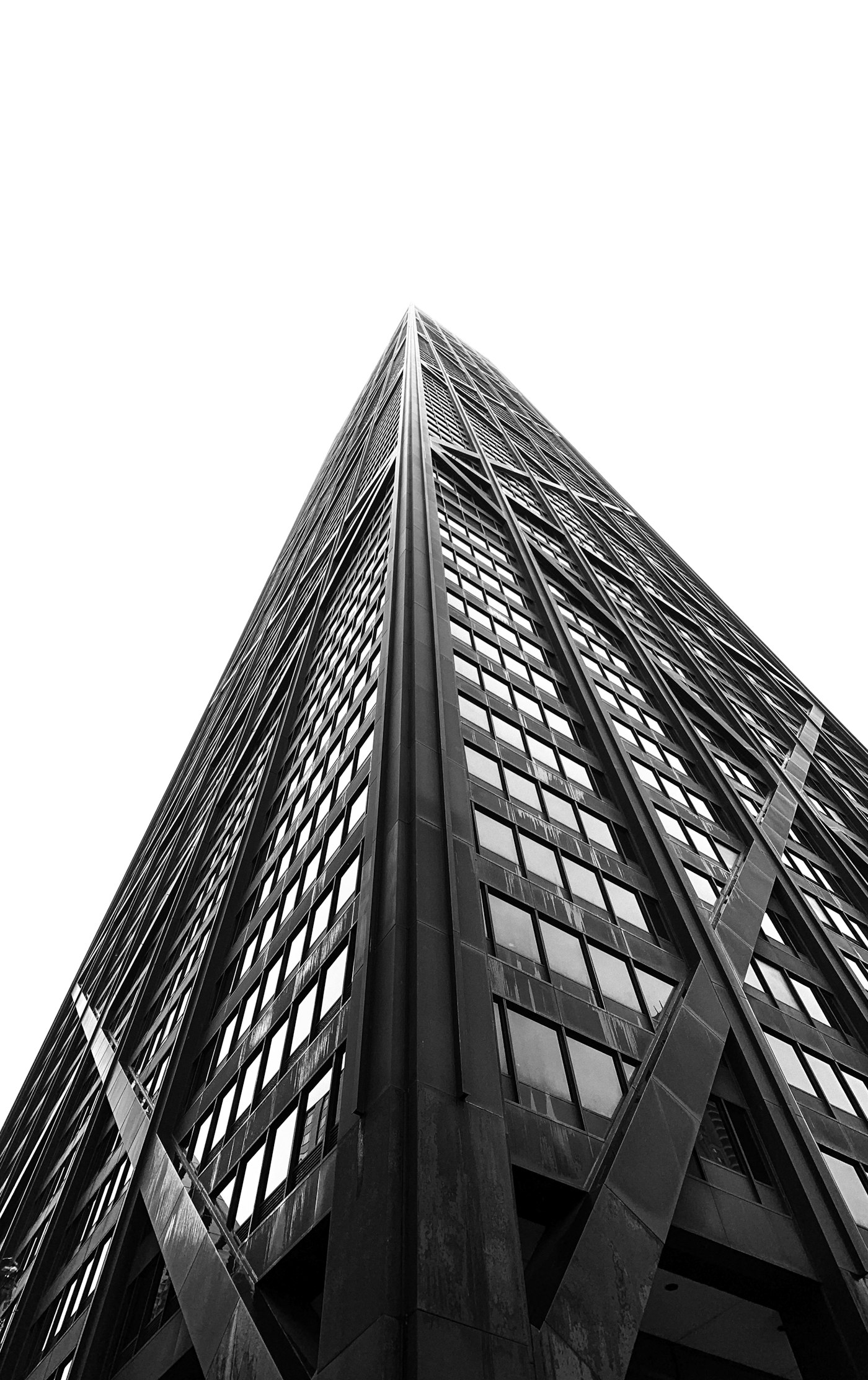 A dark glass tower rising into flat light, seen obliquely from street level